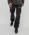 A person wearing black cargo pants with yellow accents and black PW260 sneakers by Portwest is standing against a plain white background.
