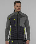 A man wearing a Portwest PW262 jacket with neon yellow zipper accents and black quilted panels stands in front of a plain grey background.