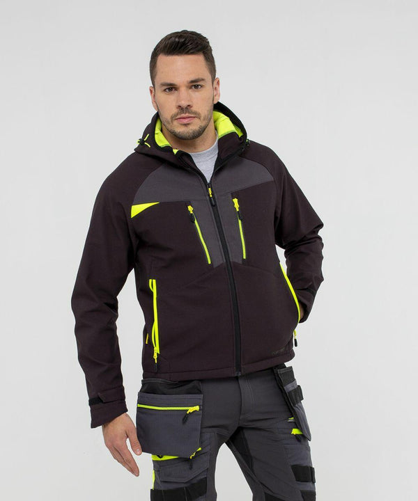 A man wearing a black and neon yellow PW263 jacket with matching pants from Portwest, standing against a plain background. The PW263 jacket has multiple zippered pockets and a hood. The pants have various pockets and straps.