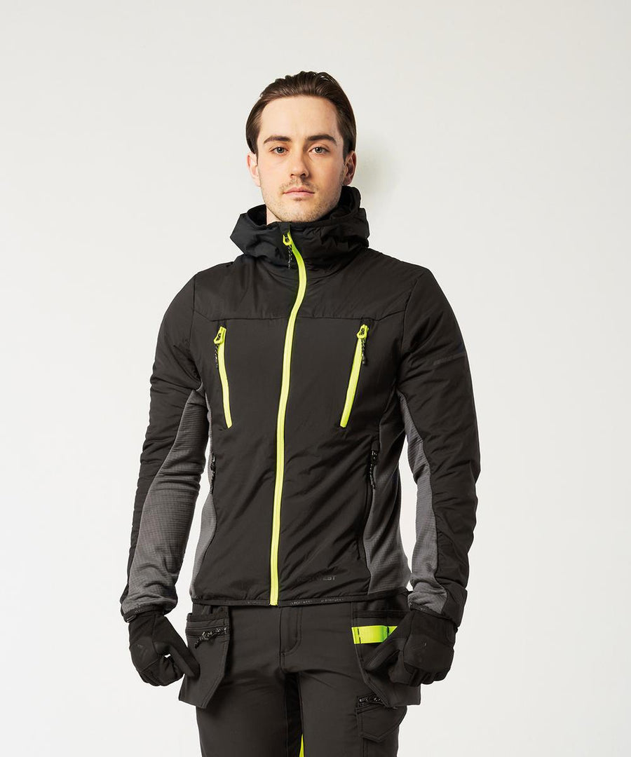 A man faces forwards against a white background, wearing the Portwest EV4 Insulated hybrid jacket (EV470) in black with neon yellow zips, matching trousers with yellow accents, and black gloves.