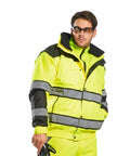 Person wearing a bright yellow Portwest PW332 high-visibility safety jacket with reflective stripes, holding an unidentified object, and wearing safety glasses.