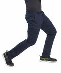 Person wearing navy blue Portwest PW363 cargo pants and black sneakers with green accents, taken mid-stride against a plain white background.