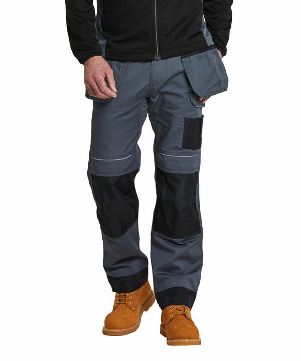 A person wearing a black jacket, PW369 by Portwest gray work pants with black knee pads, and tan work boots.