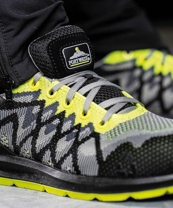 A close-up of a PW417 with a Portwest logo on the tongue. The PW417 features a gray and black mesh design with yellow accents and yellow laces.