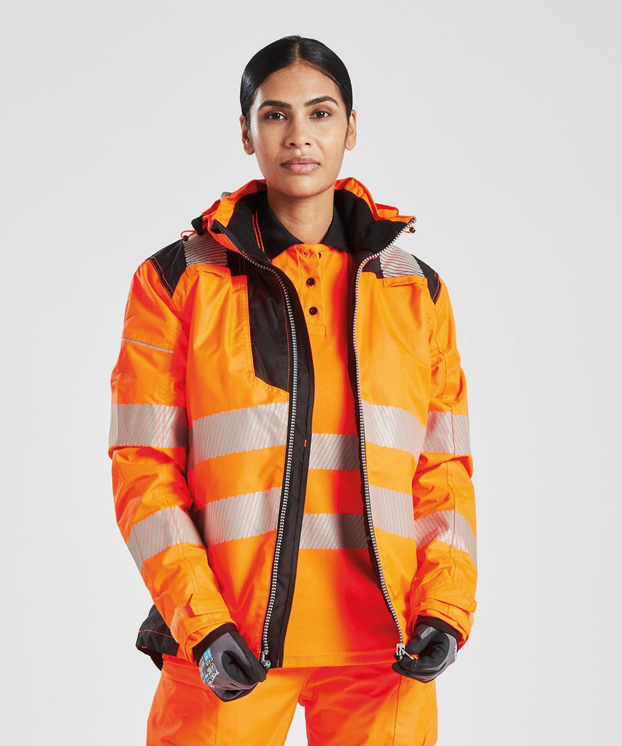A person wearing the Portwest Women's PW3 Hi-vis winter jacket (PW382) in orange, featuring silver reflective stripes and a black-trimmed hood, stands against a plain light background.