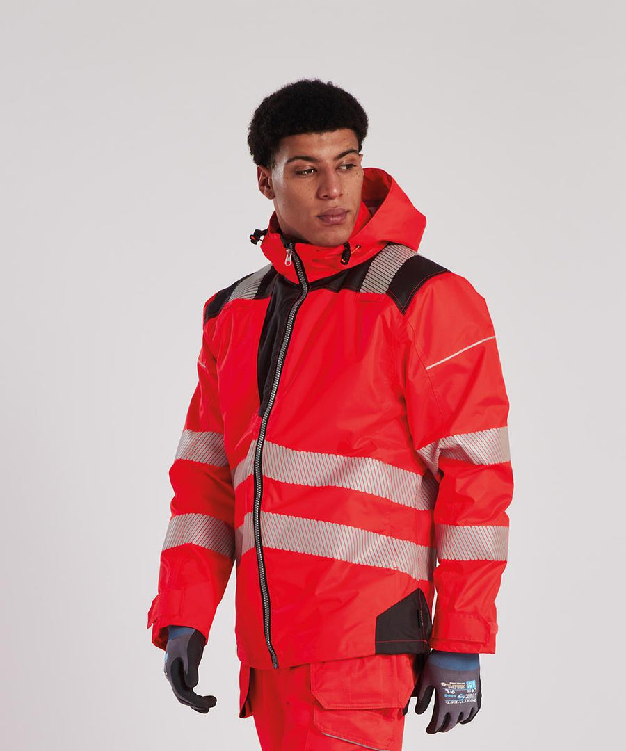 A person wearing the Portwest PW3 Hi-vis winter jacket (T400) in bright red with black accents, matching red trousers, grey gloves, and a hood stands against a plain white background.