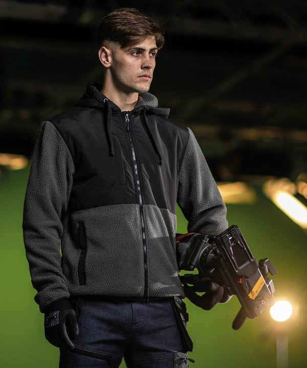 Man in a dark hoodie holding a Portwest PW511 while looking off to the side, against a dimly lit backdrop.