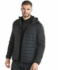 A man with short hair and a beard wearing a black Portwest PW512 puffer jacket with a hood and dark sleeves stands against a plain white background.