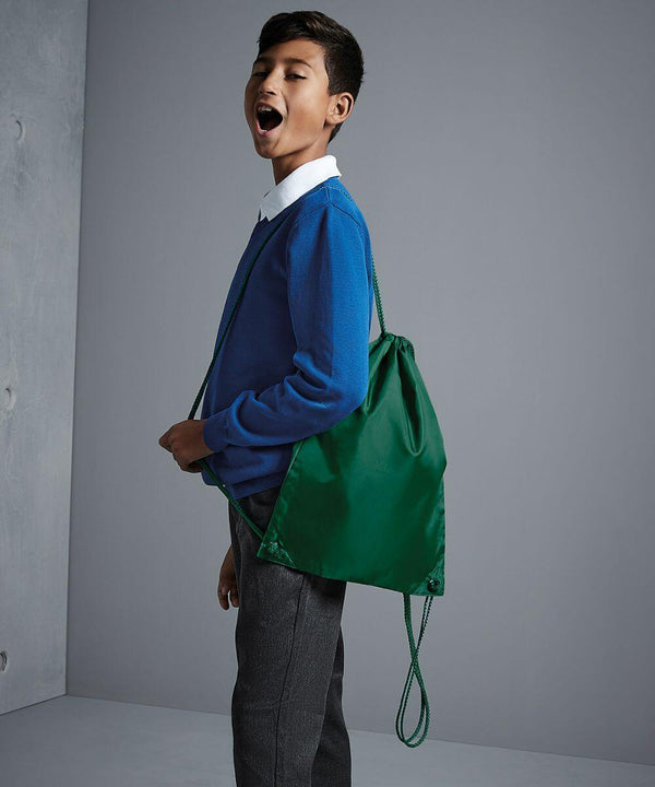 A boy wearing a blue sweater and gray pants stands with a green Quadra QD017 drawstring backpack, looking to the side with his mouth open, against a gray background.