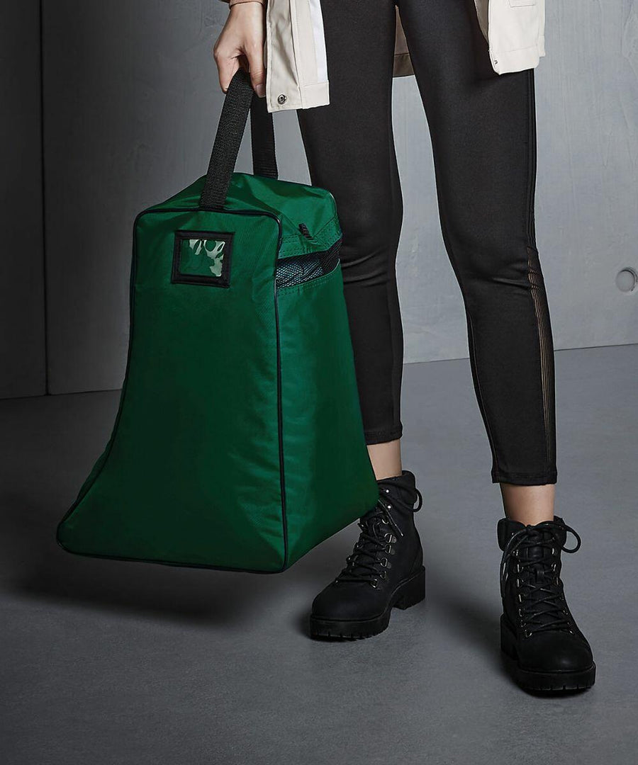 Person holding a large green Quadra QD086 tote bag with a black handle, wearing black pants and black boots.