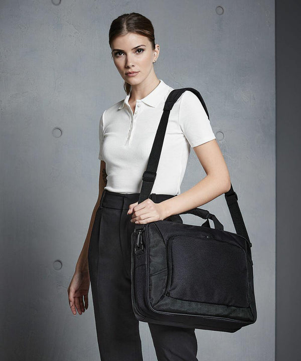 A woman in a white polo shirt and dark pants holds a Quadra QD268 shoulder bag, standing against a gray wall with circular decorations.