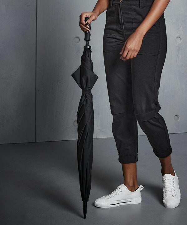 Person dressed in black pants and white sneakers holding a closed black Quadra QD360.
