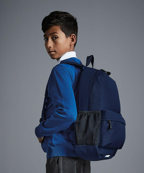 Young boy in blue sweater with white collar, grey pants, and a navy Quadra QD445 backpack, stands sideways, looking back over his shoulder against a plain, grey background.
