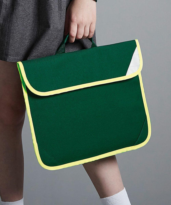 A person holds a green Quadra QD452 satchel-style school bag with yellow trim. The photo is cropped to show only the lower part of the person's body and the bag.