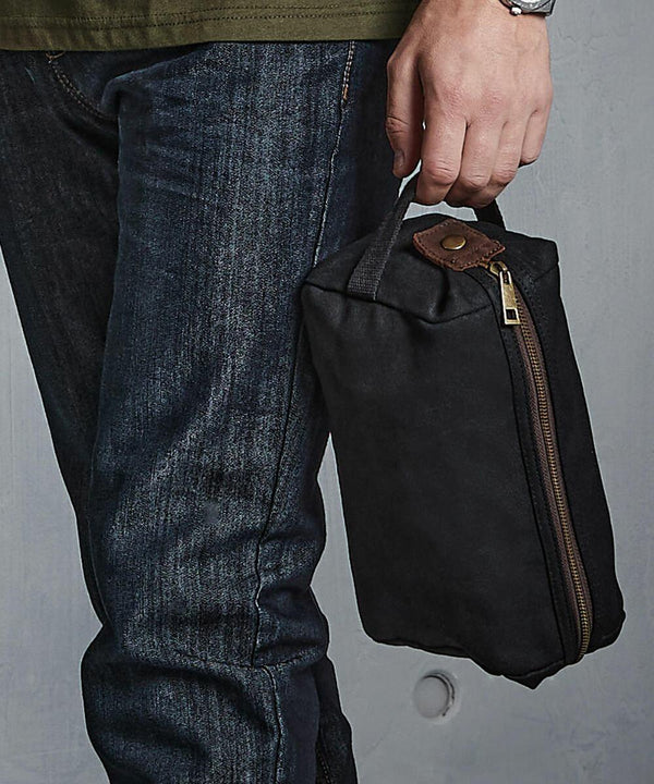 Person holding a small black zippered **Quadra QD651** bag by a handle, wearing jeans and an olive green shirt.