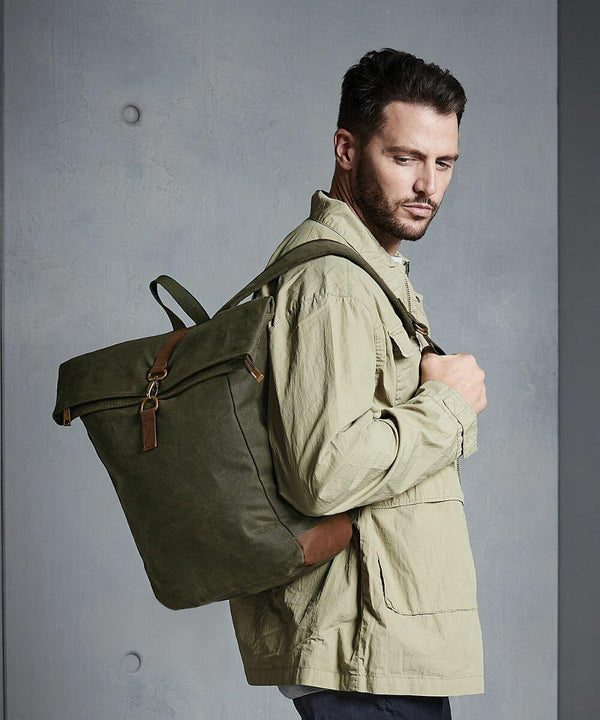 A man with short dark hair is wearing a beige jacket and carrying a large green Quadra QD655 over one shoulder, standing against a plain grey background.