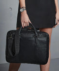 Person holding a black leather Quadra QD892 briefcase, wearing a black skirt and a silver wristwatch.