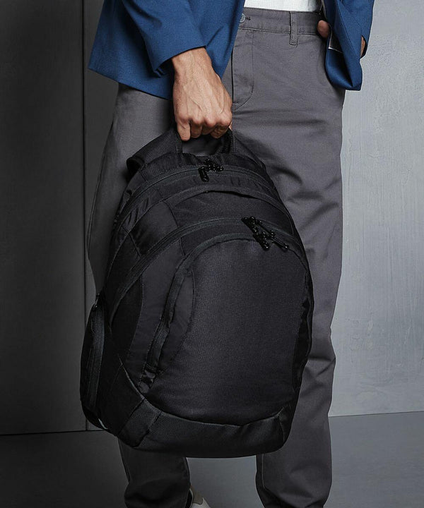A person in grey pants and a blue jacket holds a Quadra QD905 by its top handle in their right hand.