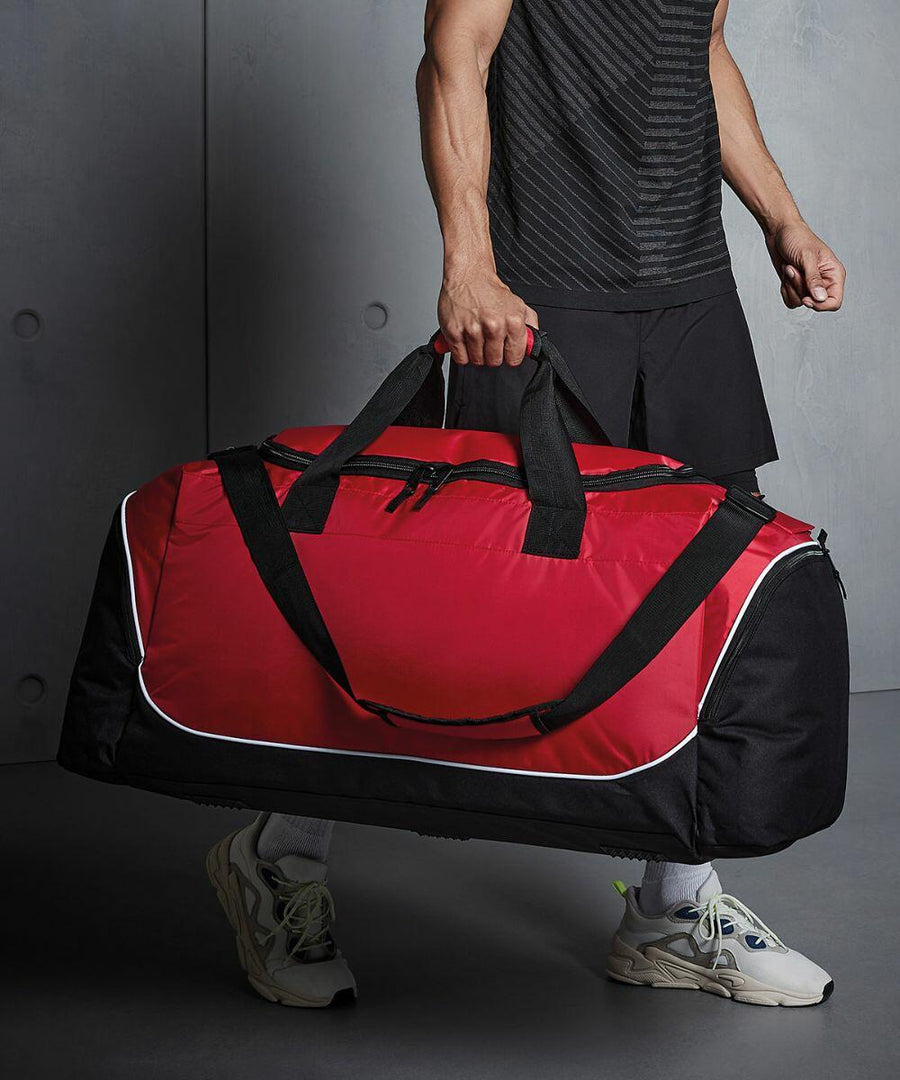 A person in athletic wear holding a large red and black Quadra QS088 duffel bag.