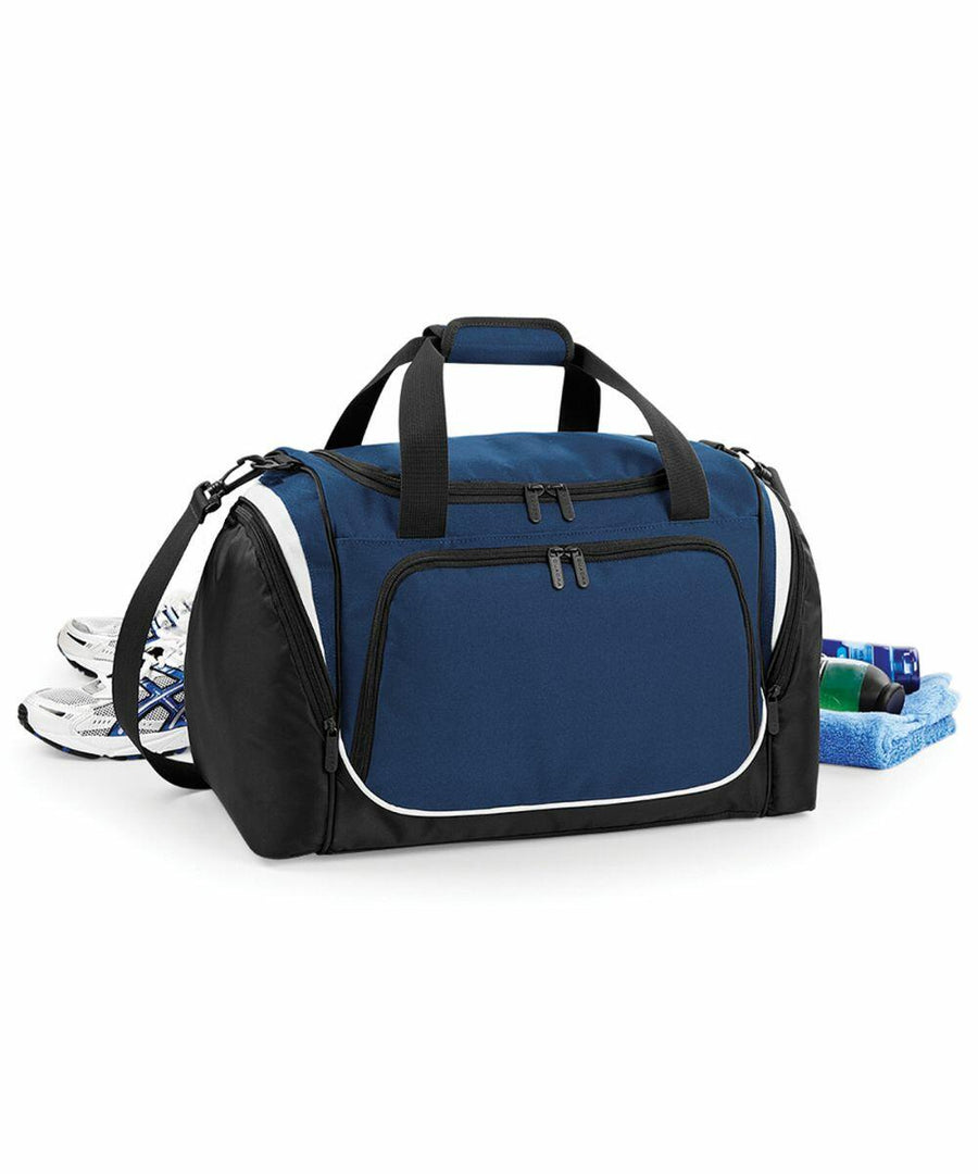 A blue and black Quadra QS277 duffel bag with black straps, surrounded by a pair of white athletic shoes, a rolled blue towel, and small toiletry bottles.