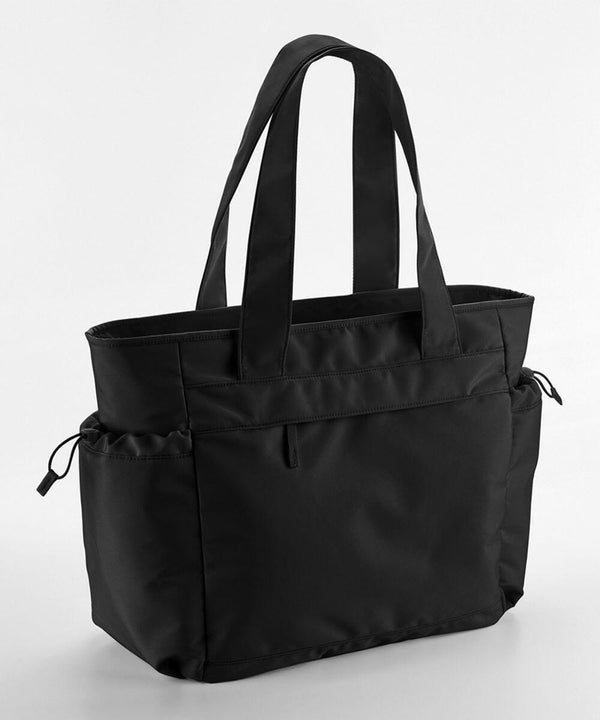 Black Quadra QS303 tote bag with two shoulder straps and multiple pockets, including two side pockets with drawstrings. The bag has a sleek design with a zippered front compartment.
