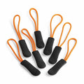 Seven Quadra QX505 zipper pulls scattered around, each showcasing a vibrant orange loop with a black textured grip.