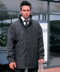A man in a Result R110A jacket stands outdoors, holding a newspaper in one hand, with a building and a car visible in the background.