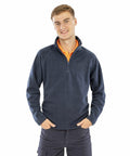 A person wearing a dark blue long-sleeve Result R112X zip-up sweater and dark pants stands with hands in their pockets, smiling at the camera.