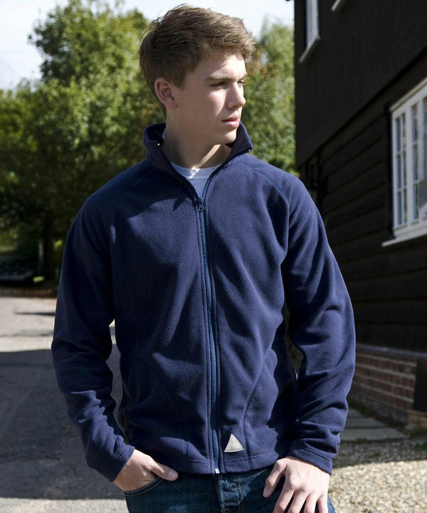 A young man in a navy blue Result R114J zip-up jacket stands outside, looking to the side with his hands in his pockets. A building and trees are visible in the background.