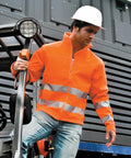 A person wearing an orange Result R117A high-visibility jacket and a white hard hat steps off industrial equipment.