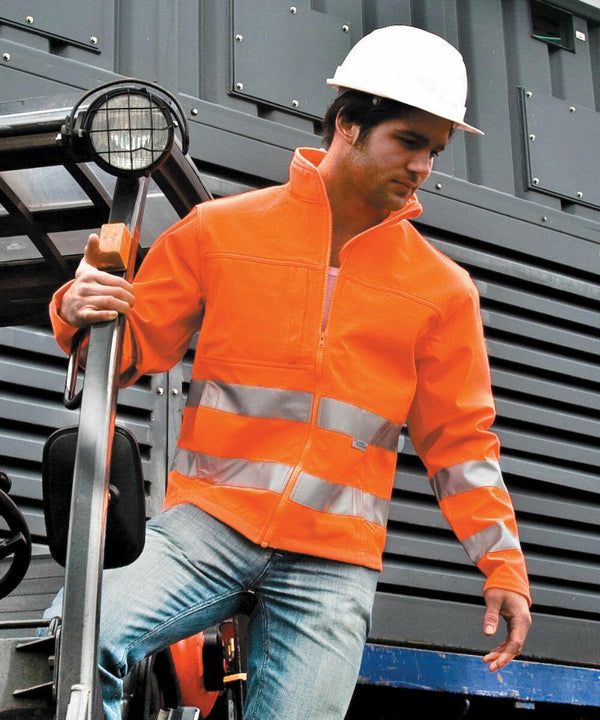 A person wearing an orange Result R117A high-visibility jacket and a white hard hat steps off industrial equipment.