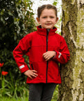 A child in a Result R121J stands next to a tree outdoors, with greenery and flowers in the background.