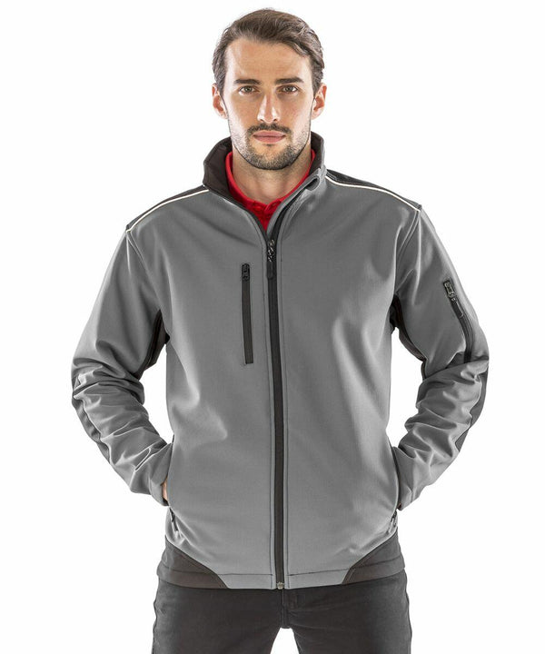 A man with long hair and a beard stands facing forward, wearing a gray zip-up jacket with black zippers and dark accents on the sides and shoulders, with his hands in the pockets. He is wearing the Result R124A.