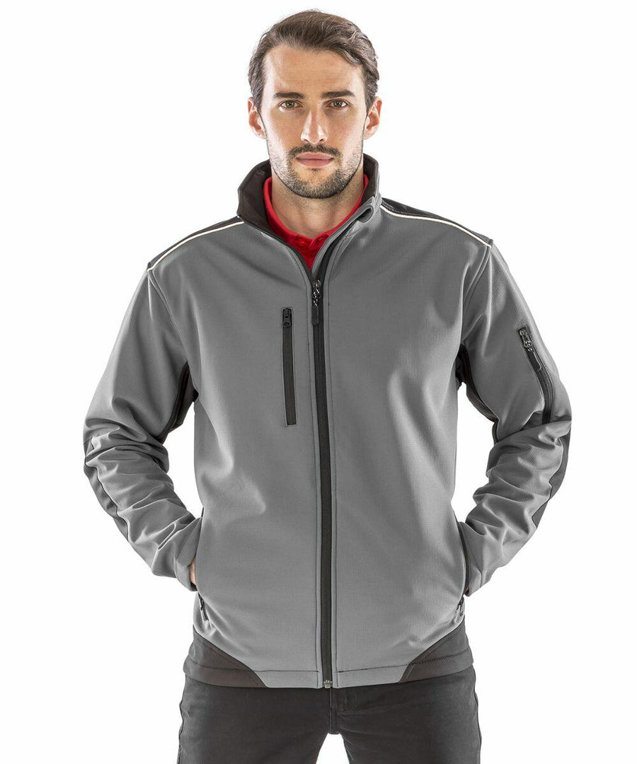 A man with long hair and a beard stands facing forward, wearing a gray zip-up jacket with black zippers and dark accents on the sides and shoulders, with his hands in the pockets. He is wearing the Result R124A.