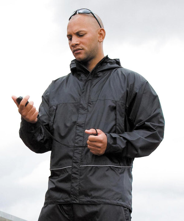 A person in a Result Waterproof 2000 midweight jacket holds a stopwatch and checks it, with sunglasses on their head and an overcast sky in the background.