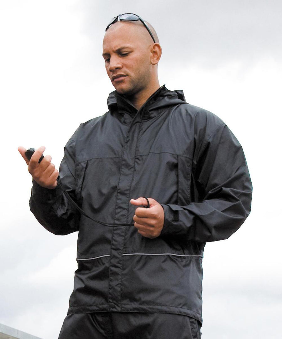 A person in a Result Waterproof 2000 midweight jacket holds a stopwatch and checks it, with sunglasses on their head and an overcast sky in the background.