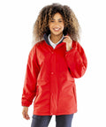 A person with curly hair wearing a red jacket and dark pants stands smiling against a white background wearing the Result R160A.