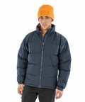 A person wearing an orange beanie, a dark Result R181M puffer jacket, and dark pants, standing against a white background.