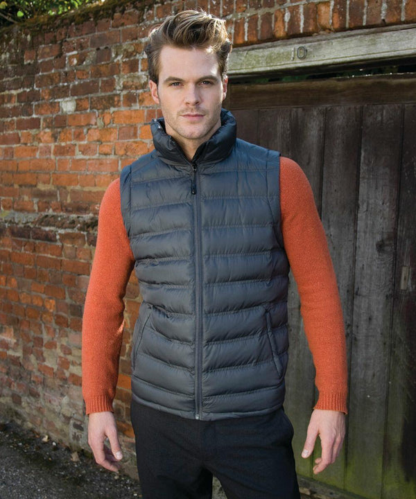 Man wearing a Result R193M over an orange long-sleeve shirt stands in front of a brick wall and wooden door.