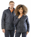 A man and woman in black quilted jackets and orange shirts stand side by side, both smiling, against a plain white background, wearing the R195X from Result.