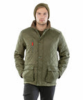 A person wearing a green Result R196X quilted jacket with multiple pockets and a beanie hat is standing with hands in pockets, facing the camera.