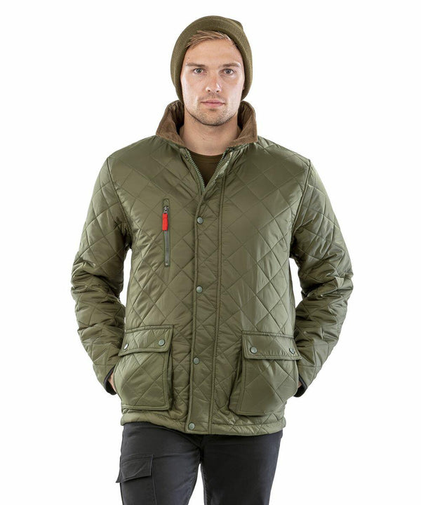 A person wearing a green Result R196X quilted jacket with multiple pockets and a beanie hat is standing with hands in pockets, facing the camera.