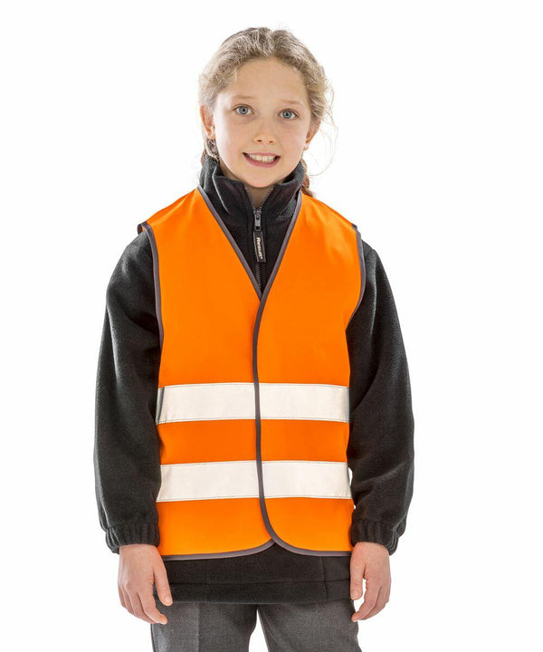 Young girl wearing a Result R200J safety vest with reflective stripes, standing against a plain white background, smiling slightly.