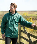 A man stands outdoors, resting one arm on a wooden gate. He is wearing a green Result R203X windbreaker jacket and looking to the side.
