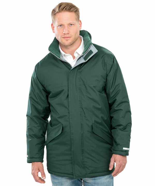 A man wearing a forest green R207X winter coat with a high collar and front pockets by Result over a white shirt, standing against a plain white background.