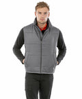 A person standing, wearing a Result R208X gray puffer vest over a black long-sleeved shirt and black pants.