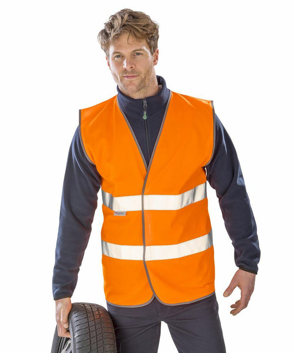 A person wearing an orange Result R211A safety vest over a navy blue sweatshirt holds a tire in one hand.