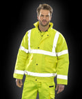 Man wearing a bright yellow Result R217X high-visibility jacket and matching pants, standing against a dark background.