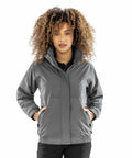 A person with curly hair is wearing a gray Result R221F jacket with hands in the pockets, standing against a plain white background.