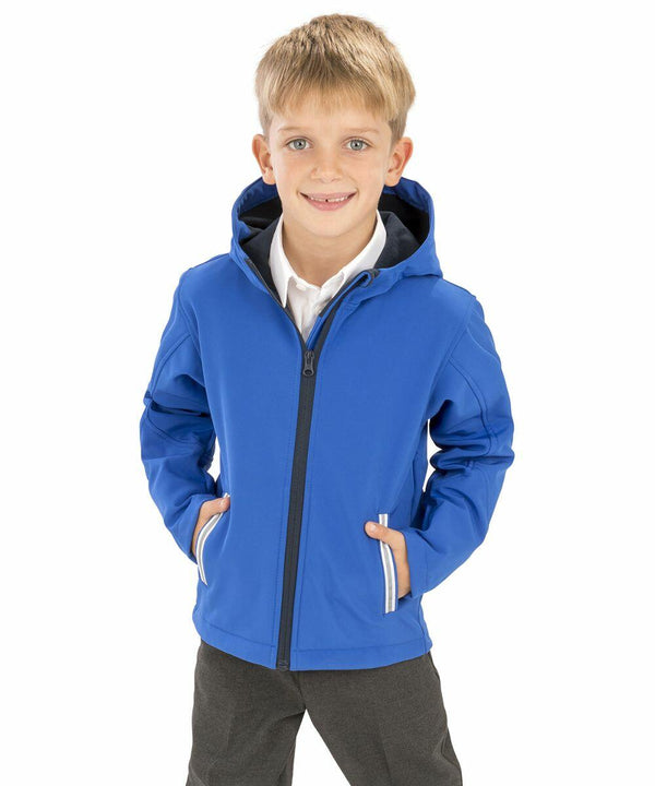 A young boy in a blue Result R224J hooded jacket and grey pants stands with his hands in his pockets, smiling.